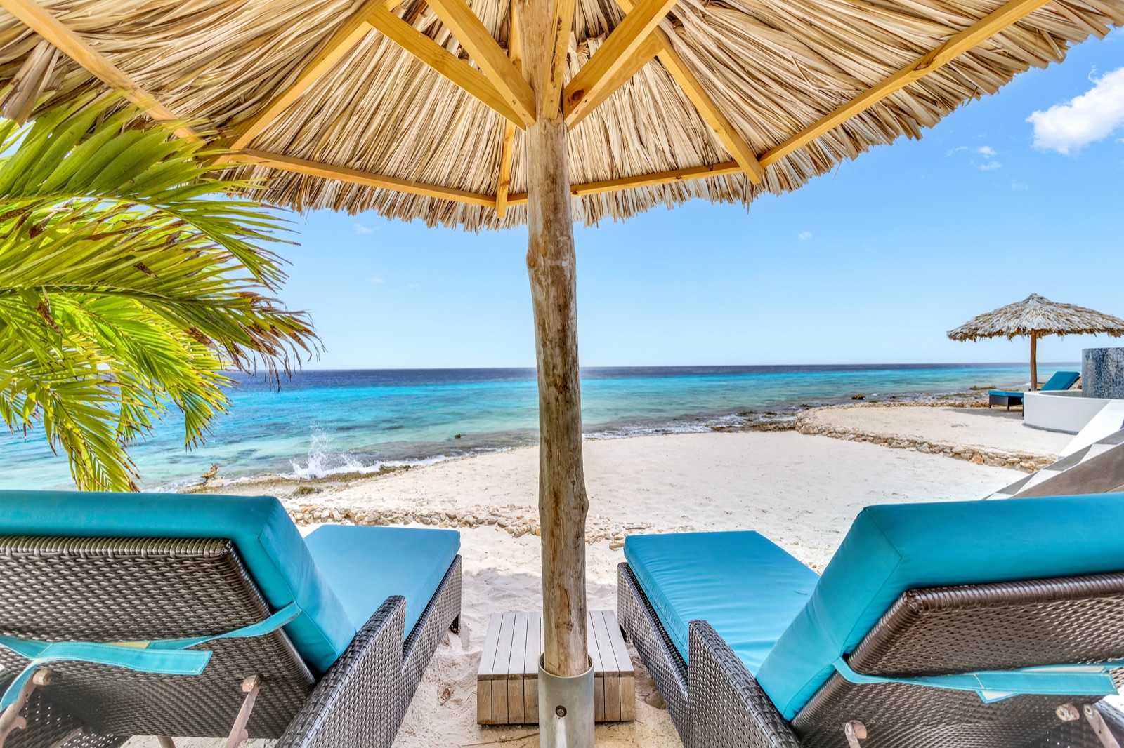 Shaded loungers on the sandy terrace beside Bonaire’s clear blue water